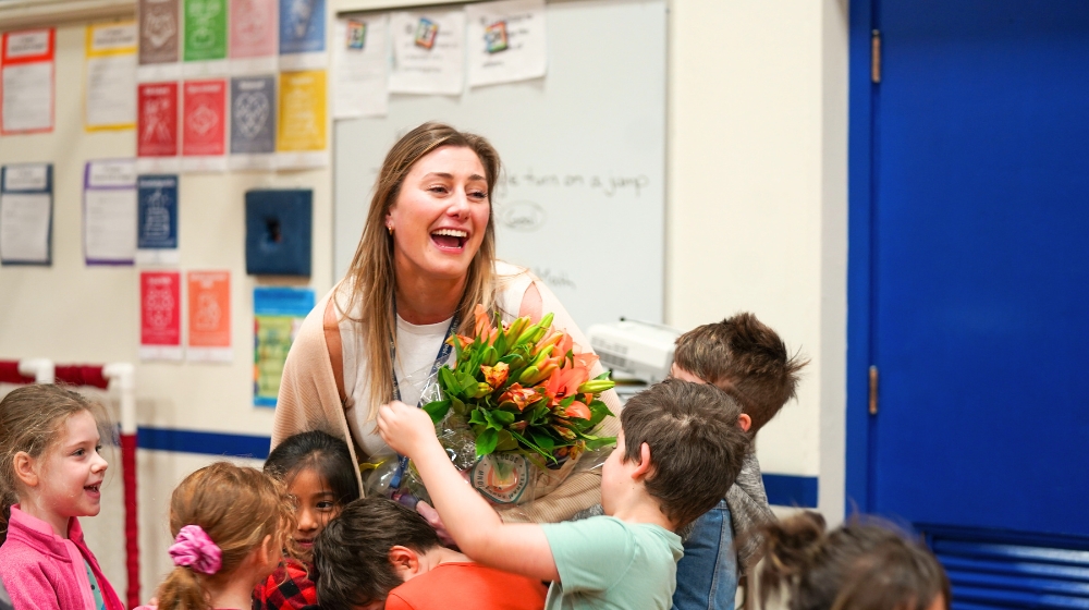 Staff member holding flowers laughs and students gather around to celebrate an award